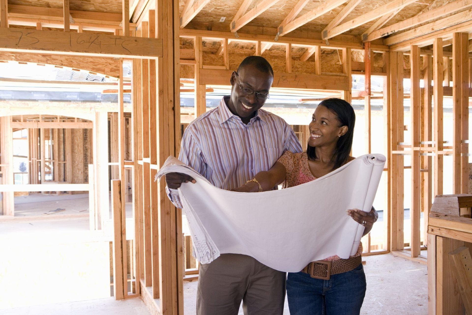 Young African American couple in a newly framed house looking at the architect's blueprints