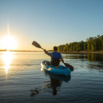 An adult male is kayaking at sunset on a peaceful fall evening in a serene environment